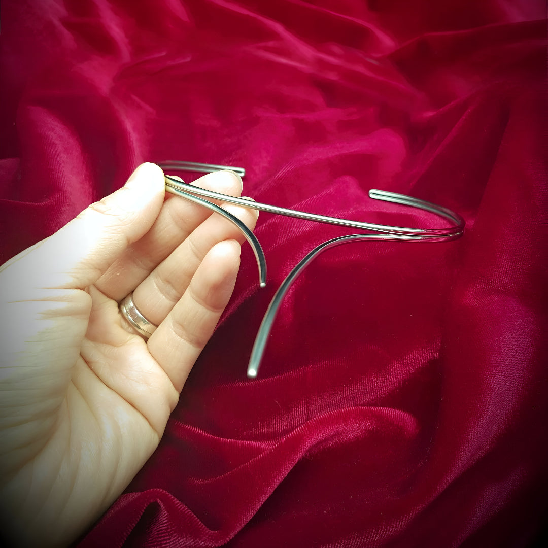 Présentation du Collier Torque Courbes Enlacées en argent, tenu à la main devant fond rouge
