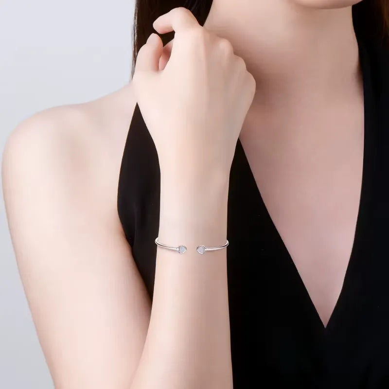 Bracelet jonc double cœur argenté Elvaëlys en argent 925 plaqué or blanc et moissanites porté au poignet d'une femme vue de face.