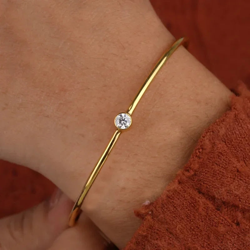 Jonc solitaire fin en argent 925 plaqué or jaune et diamant serti clos porté au poignet d'une femme vue de proche.