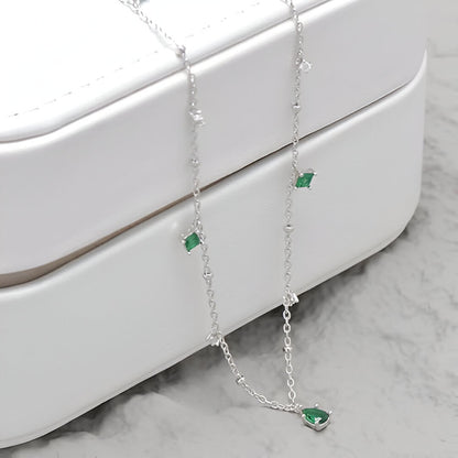 Collier pendentif à charms en argent 925 plaqué or blanc et zircons naturels verts et blancs posé sur le côté d'un écrin.