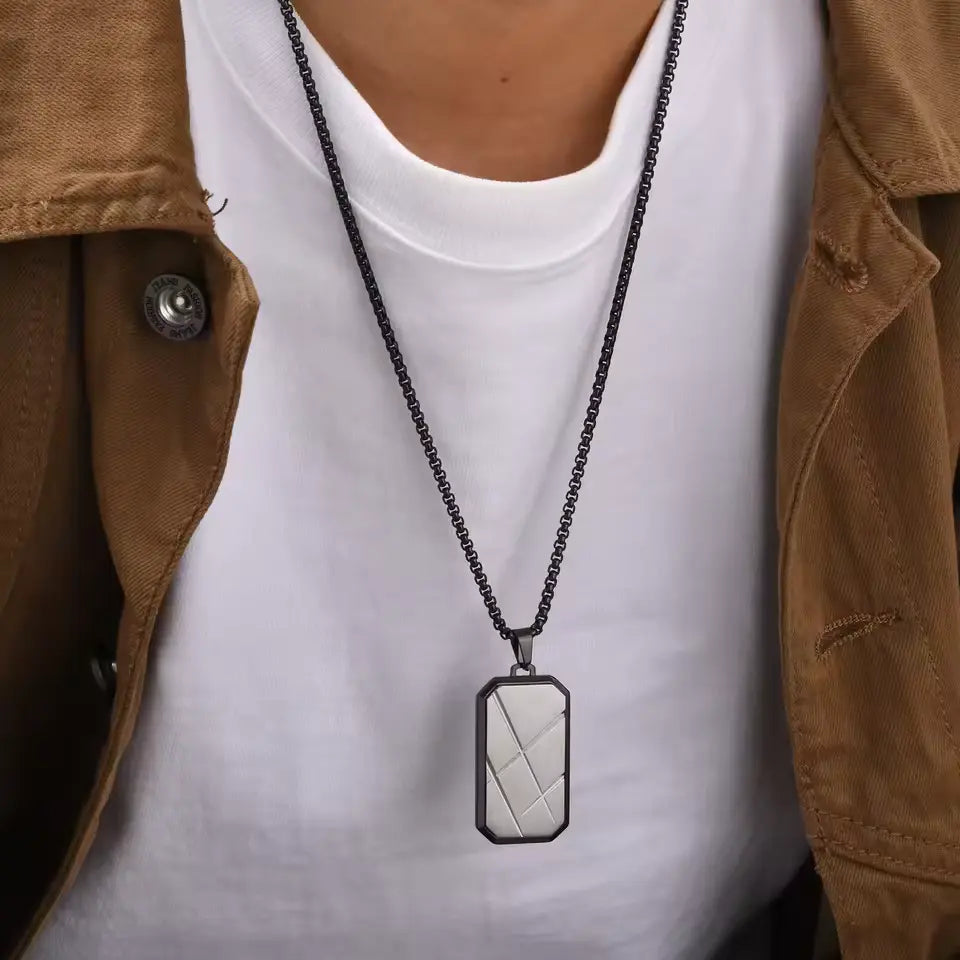 Pendentif amulette en acier plaqué or blanc porté au cou d'un homme vue de face.