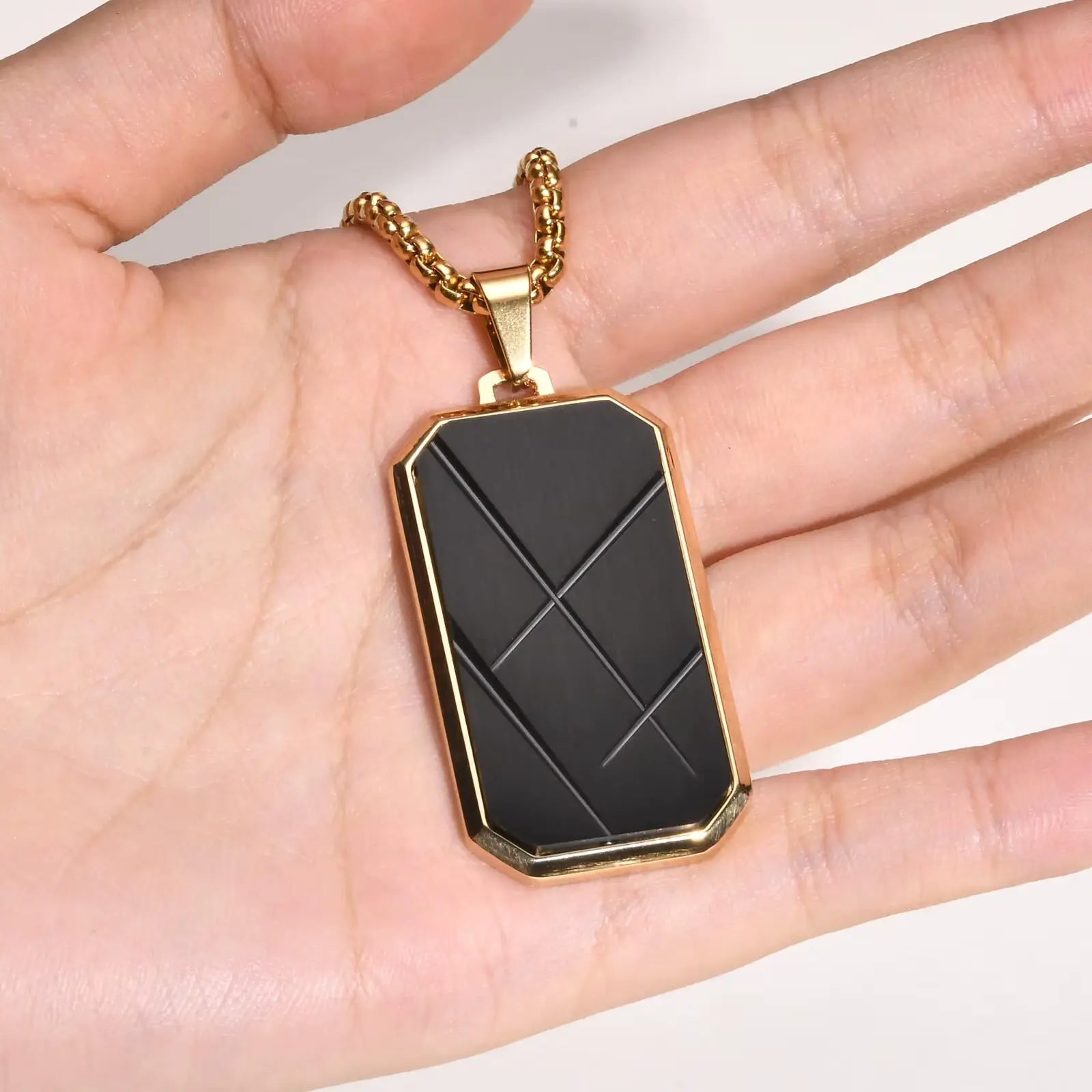 Pendentif amulette en acier inoxydable doré sur une main vue de face.