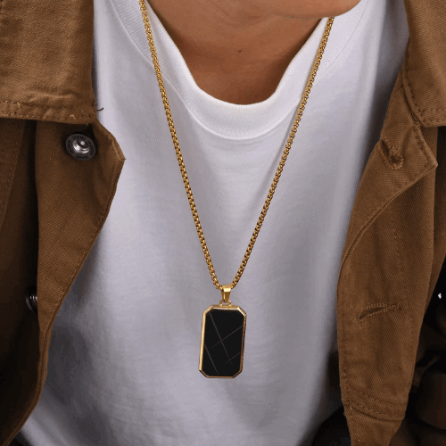 Pendentif amulette en acier inoxydable doré porté au cou d'un homme vue de face.