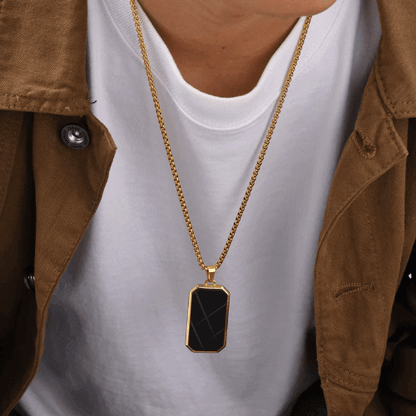 Pendentif amulette en acier inoxydable doré porté au cou d'un homme vue de face.