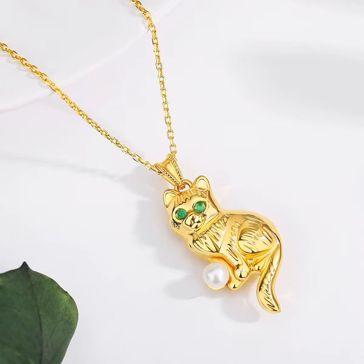 Pendentif chat Cathy en or jaune 18K serti d'une perle naturelle ronde et de péridots ronds vue de proche.
