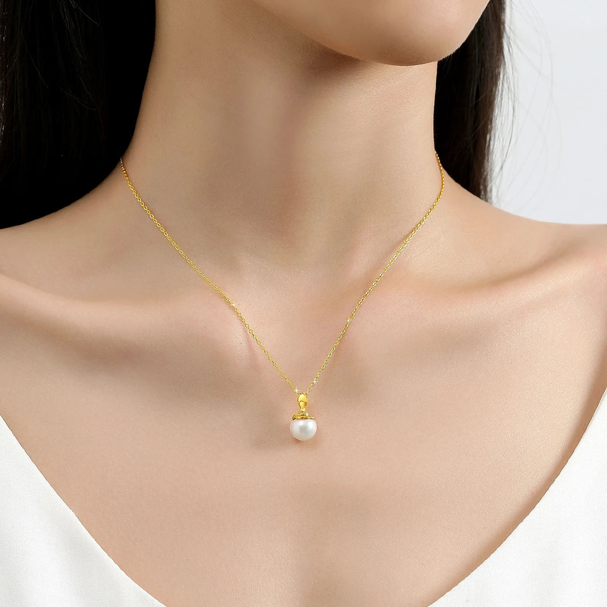 Pendentif cobra doré Sarah en or jaune 18K rayonnant et perle naturelle nacrée porté au cou d'une femme vue de loin.