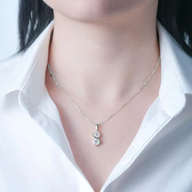 Collier pendentif courbé en argent 925 plaqué or blanc et double moissanites serties invisible porté au cou d'une femme vue de proche.