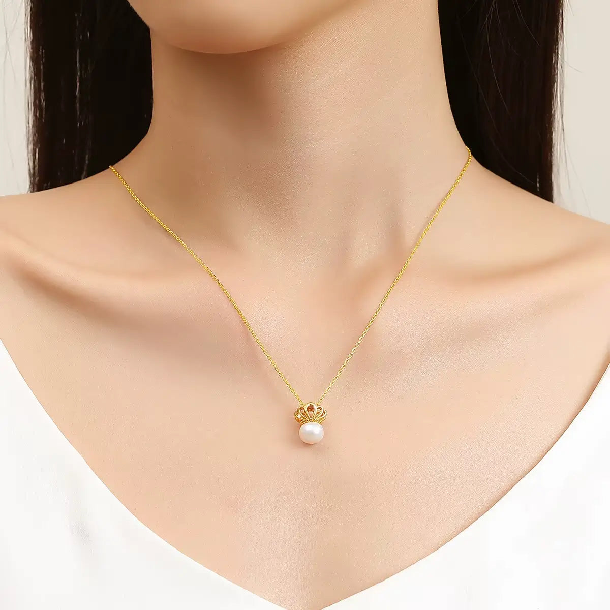 Pendentif couronne de la reine Elisabeth en or jaune 18K et perle ovale porté au cou d'une femme vue de face.