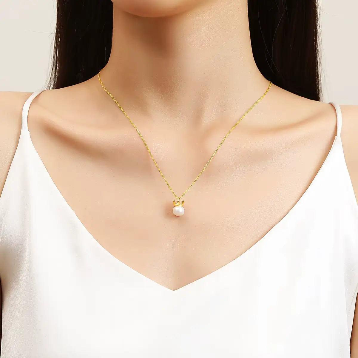 Pendentif couronne du roi Louis en or jaune 18K rayonnant et perle naturelle porté au cou d'une femme vue de loin.