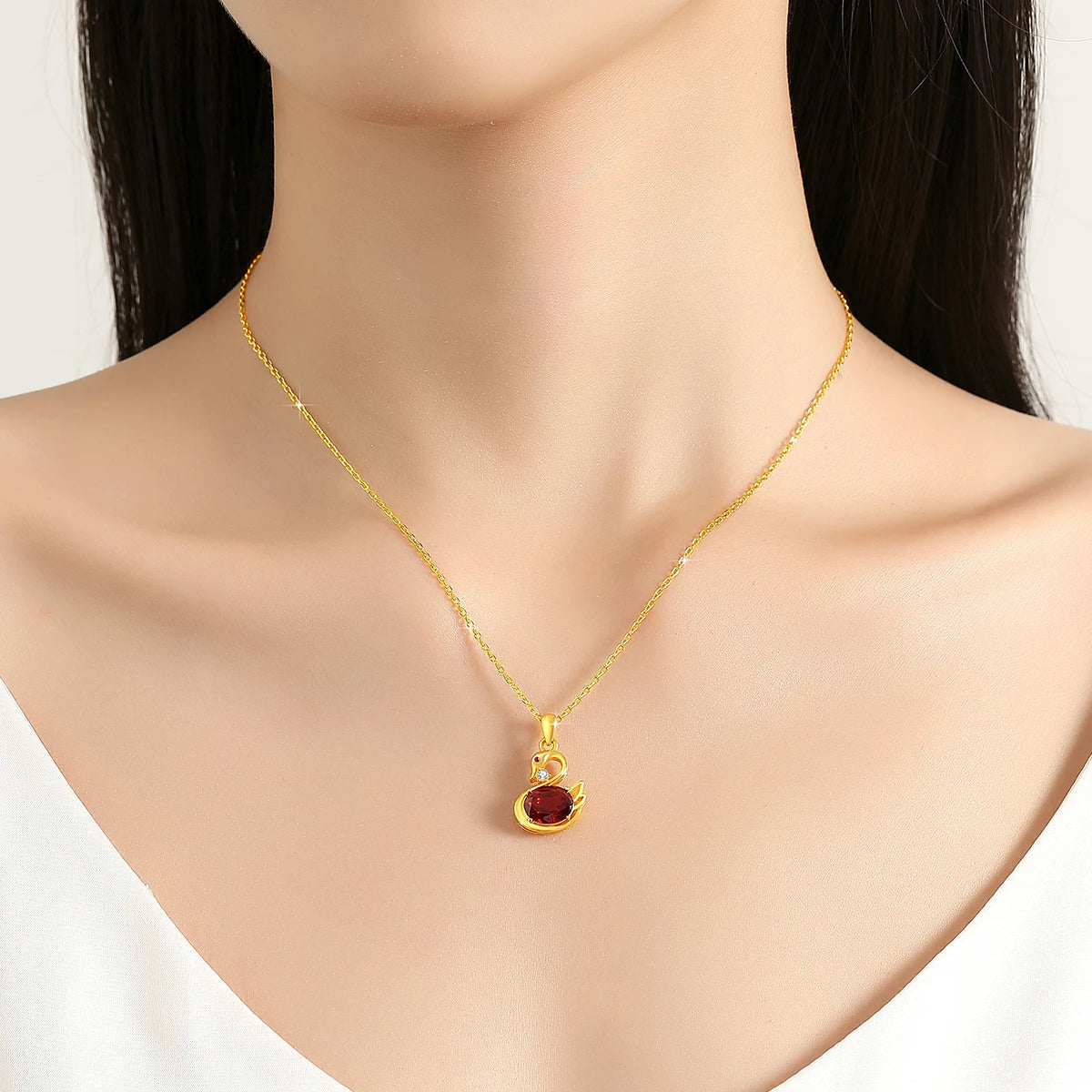Pendentif cygne grenat romantique en or jaune 18K serti d'un diamant et d'un rubis porté au cou d'une femme vue de face.