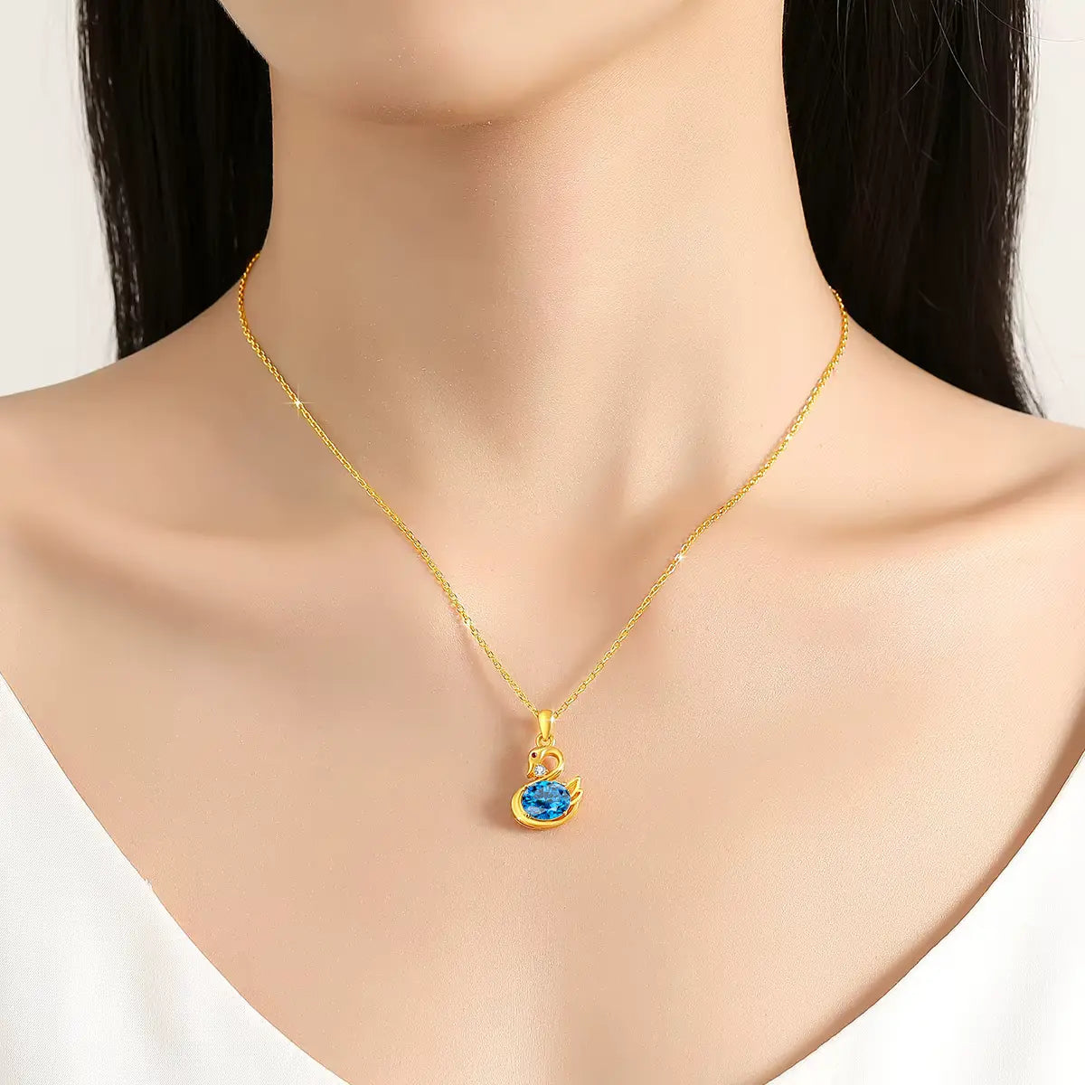 Pendentif cygne topaze radieuse en or jaune 18K orné d'un rubis et d'un diamant porté au cou d'une femme.