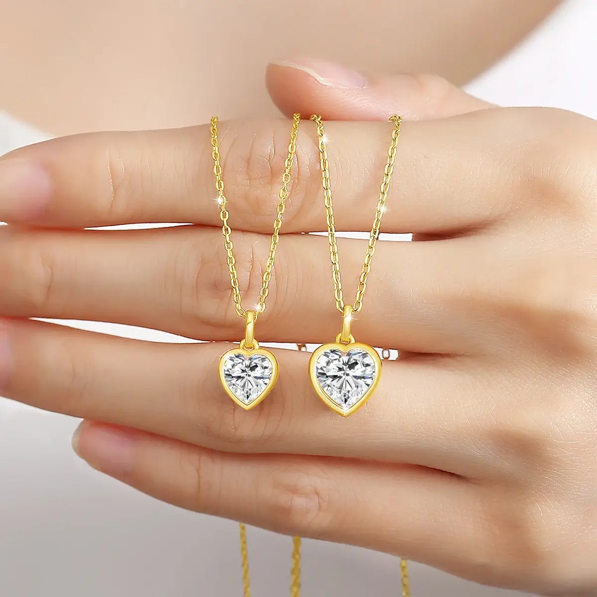 Variantes 1CT et 2CT du collier pendentif diamant cœur serti clos Lotso en or jaune 14K sur la main d'une femme vue de face.