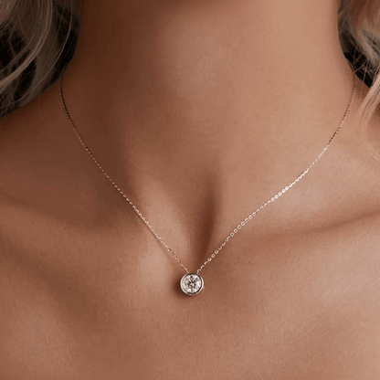 Pendentif diamant serti clos 1ct en or blanc 18K discret porté au cou d'une femme vue de proche.