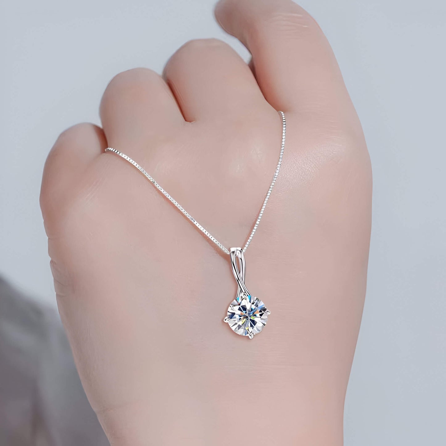 Collier pendentif echevêtré en argent 925 plaqué or blanc et moissanite solitaire scintillante sur le dos d'une main vue de face.