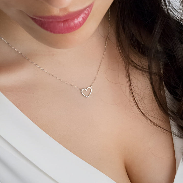 Collier pendentif fantaisie cœur en acier platiné plaqué or blanc porté au cou d'une femme.