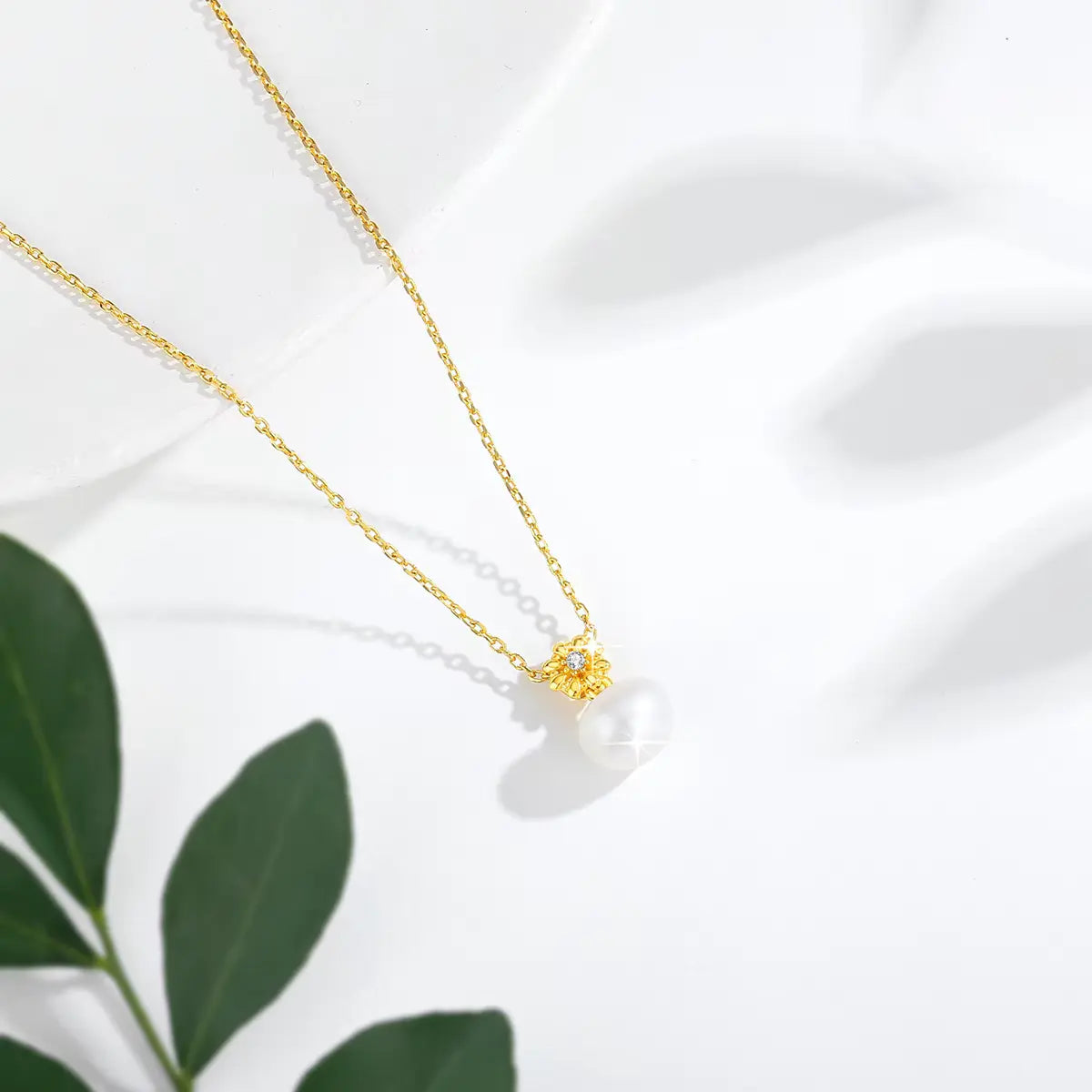 Pendentif fleur de marguerite Solénia en or jaune 18K orné d'un diamant étincelant et d'une perle naturelle vue du dessus.