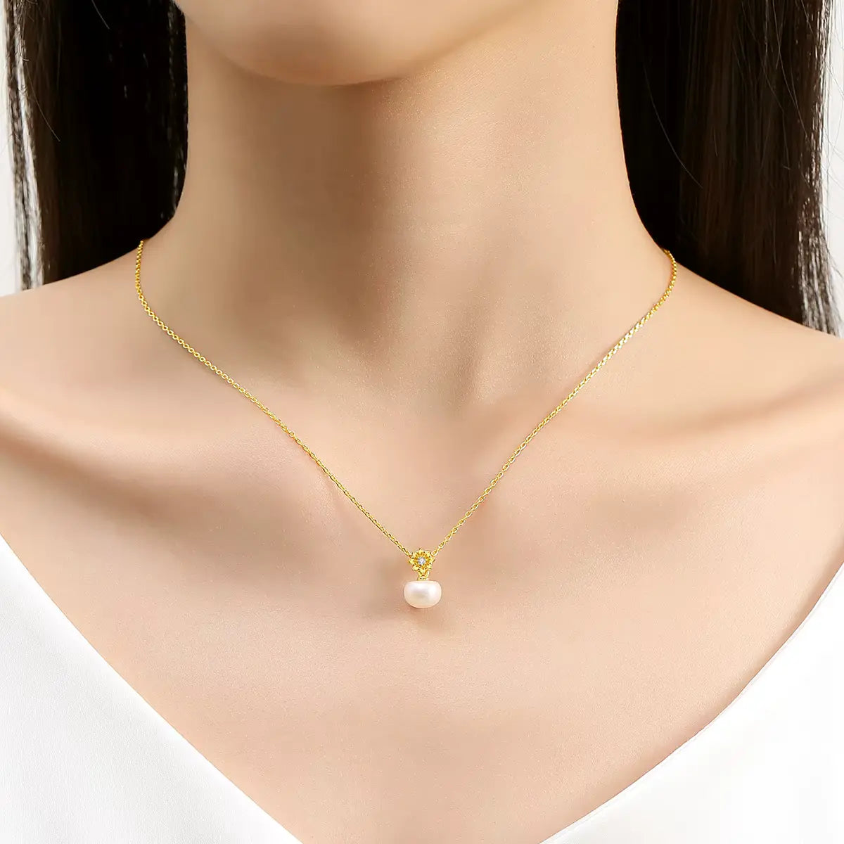 Pendentif fleur de marguerite Solénia en or jaune 18K orné d'un diamant scintillant et d'une perle naturelle porté au cou d'une femme vue de face.