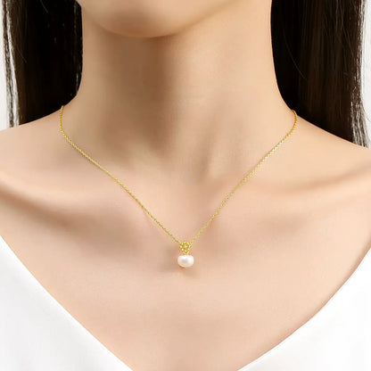 Pendentif fleur de marguerite Solénia en or jaune 18K orné d'un diamant scintillant et d'une perle naturelle porté au cou d'une femme vue de face.