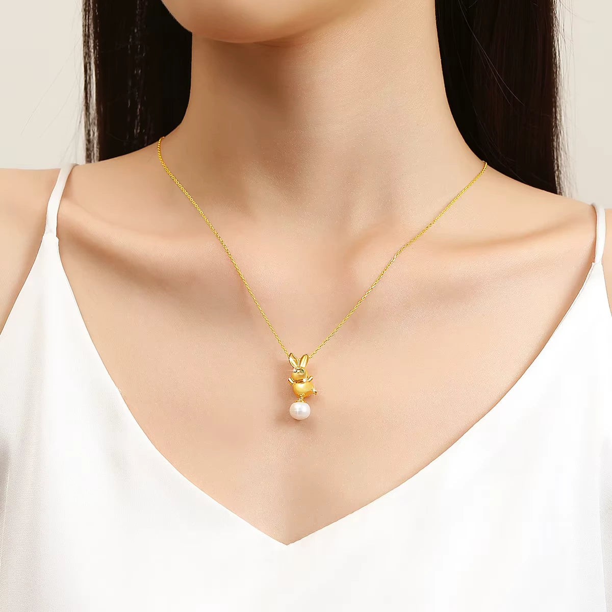 Pendentif lapin Bunny en or jaune 18K  rayonnant orné d'une perle ovale et de péridots verts porté au cou d'une femme vue de loin.