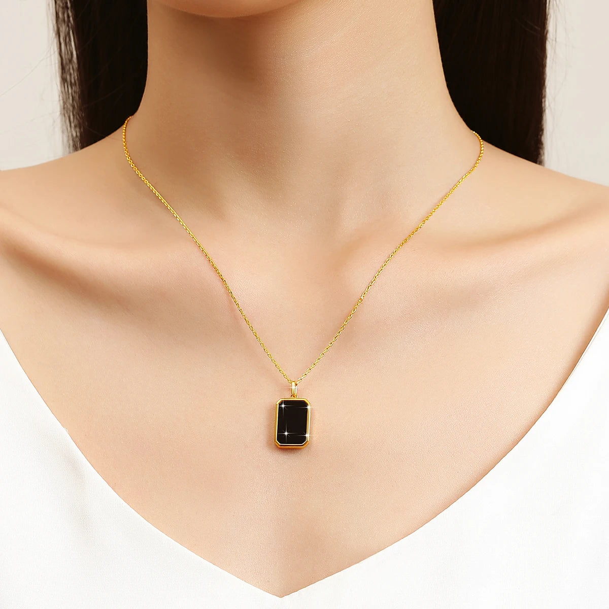 Pendentif médaillon rectangulaire en or jaune et onyx noir porté au cou d'une femme.