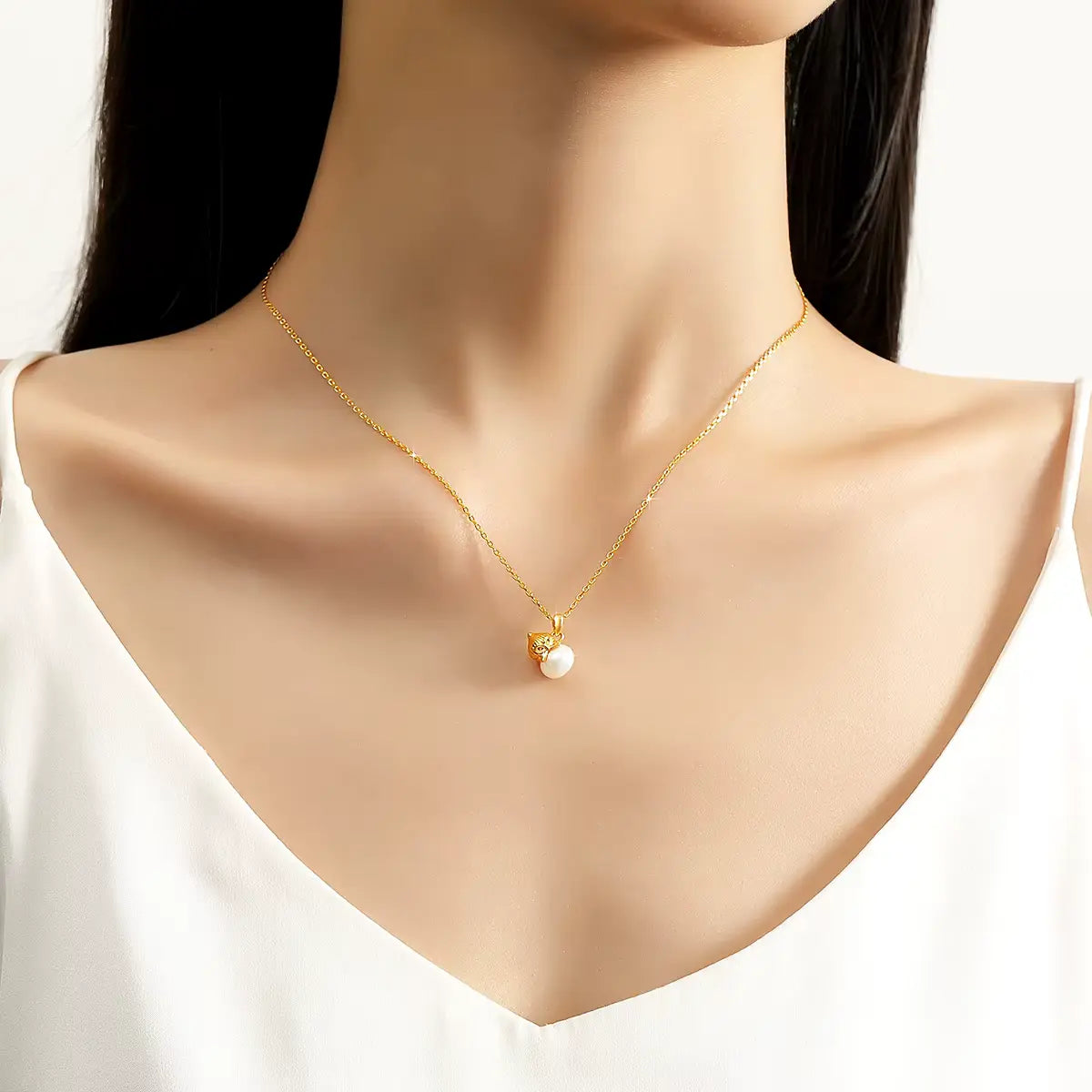 Pendentif nœud papillon en or jaune et perle porté au cou d'une femme vue de face.