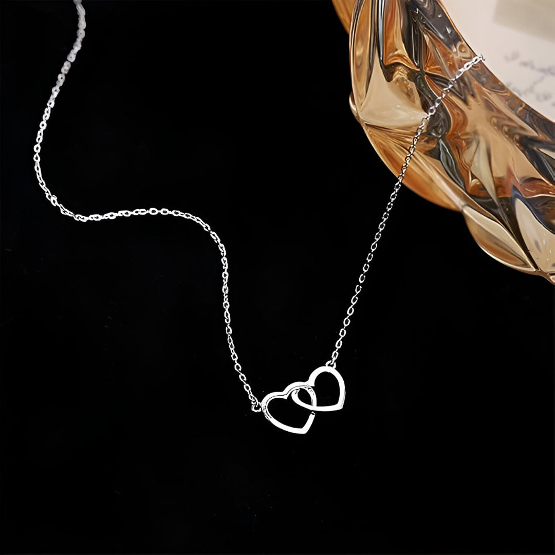 Collier pendentif fantaisie paire de cœurs en acier plaqué or blanc étalé.