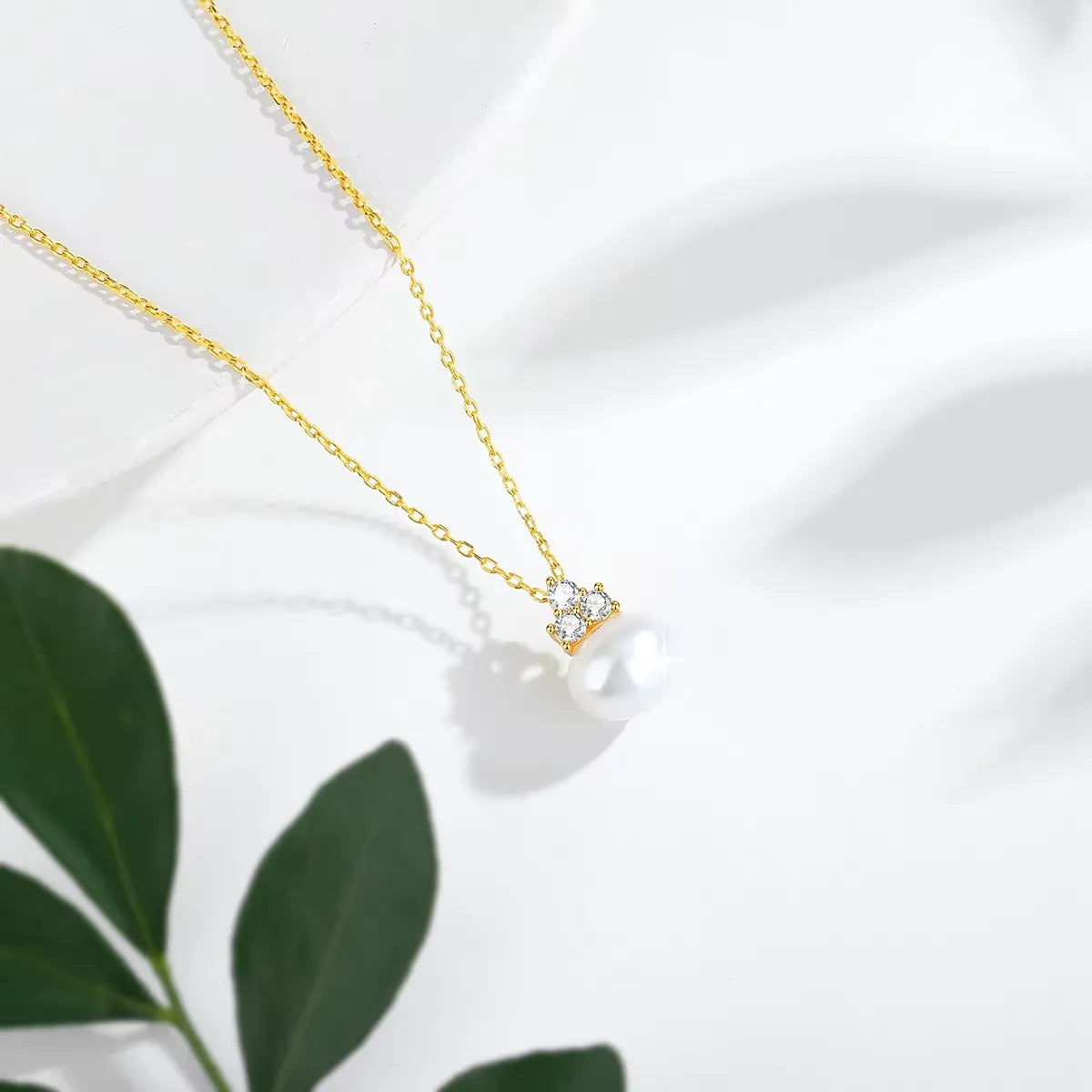 Pendentif perle solitaire en or jaune et trio de diamants synthétiques vue du dessus.