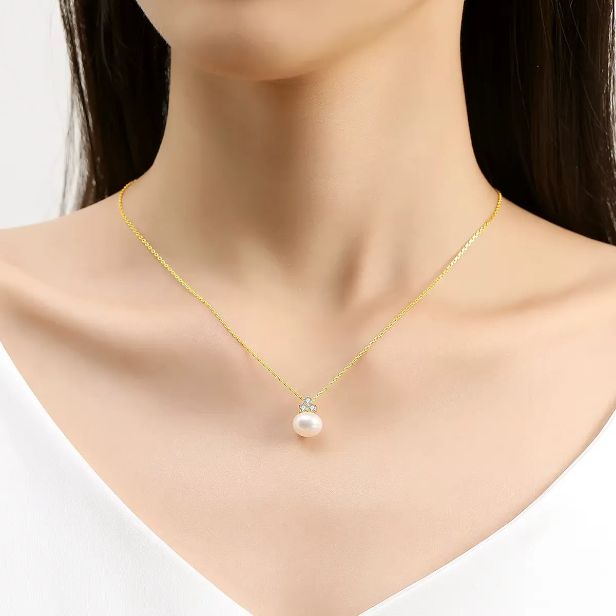 Pendentif perle solitaire en or jaune et trio de diamants synthétiques porté au cou d'une femme.