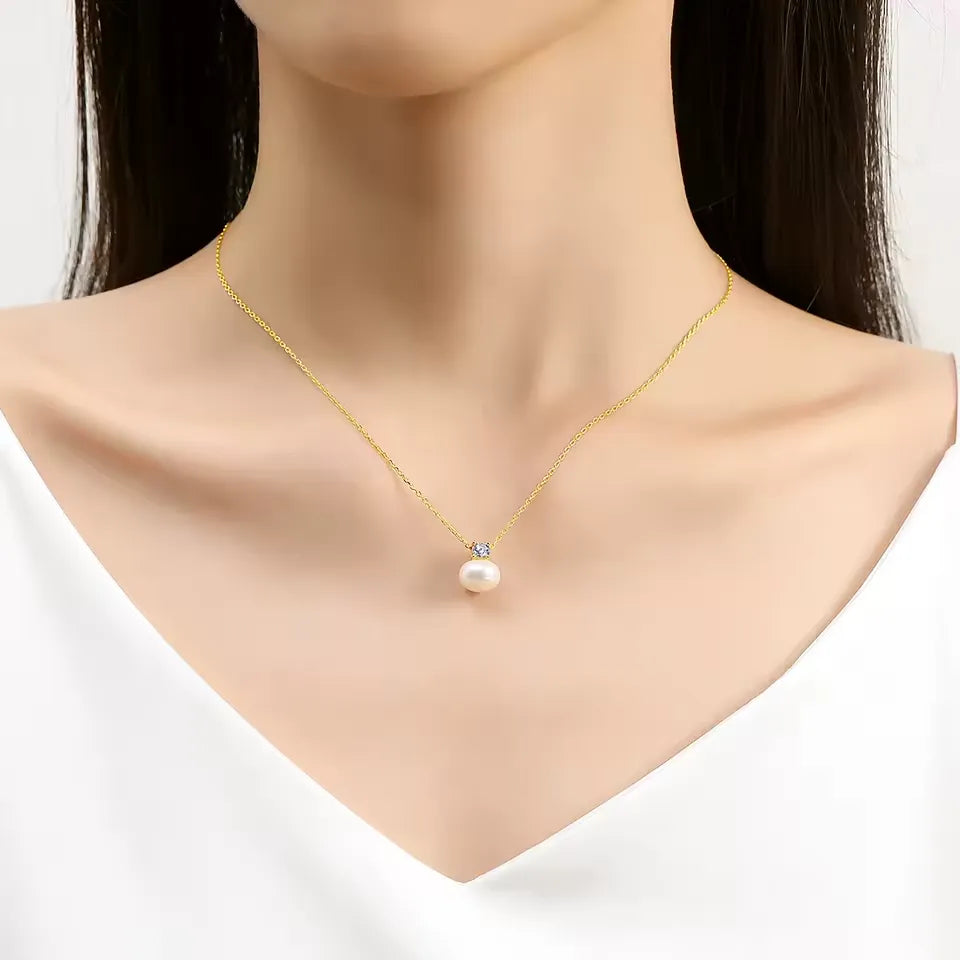 Pendentif perle solitaire nacrée Marie en or jaune 18K et diamant scintillant serti griffes porté au cou d'une femme vue de loin.