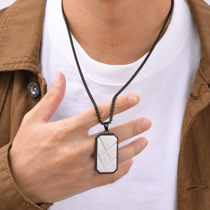Pendentif rectangulaire unisexe plaqué or blanc en acier inoxydable noir porté au cou d'un homme vue de proche.