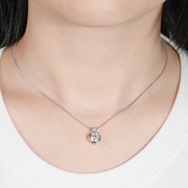 Pendentif serti clos en or blanc et diamants synthétiques porté au cou d'une femme vue de face.