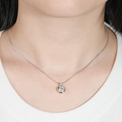 Pendentif serti clos en or blanc et diamants synthétiques porté au cou d'une femme vue de face.