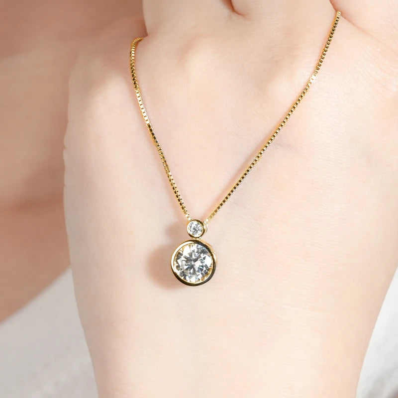 Pendentif serti clos en or jaune et diamants synthétiques sur une main de femme.