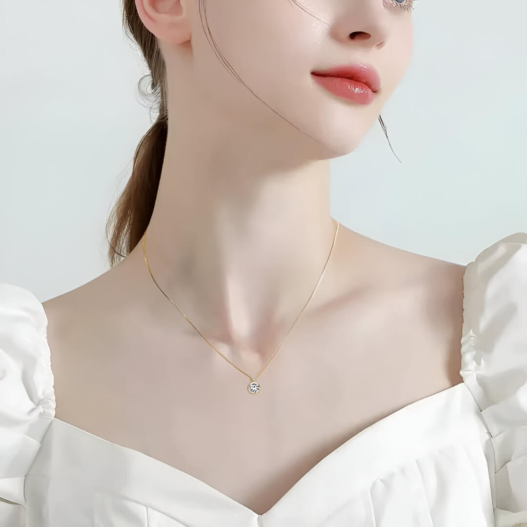 Pendentif serti clos en or jaune et diamants synthétiques porté au cou d'une femme vue de loin.