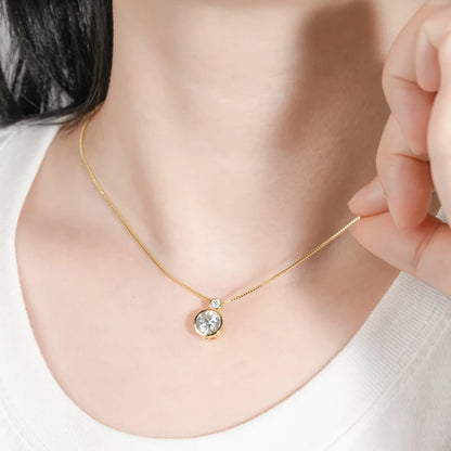 Pendentif serti clos en or jaune et diamants synthétiques porté au cou d'une femme.