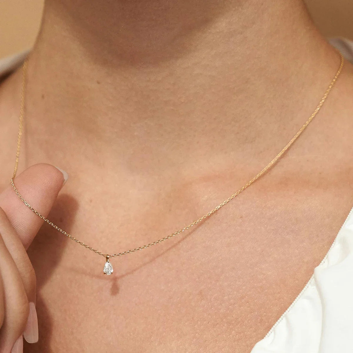 Pendentif solitaire diamant scintillant taille goutte serti trois griffes Emelynn en or jaune 14K porté au cou d'une femme vue de loin.