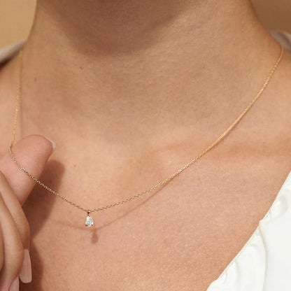Pendentif solitaire diamant scintillant taille goutte serti trois griffes Emelynn en or jaune 14K porté au cou d'une femme vue de loin.