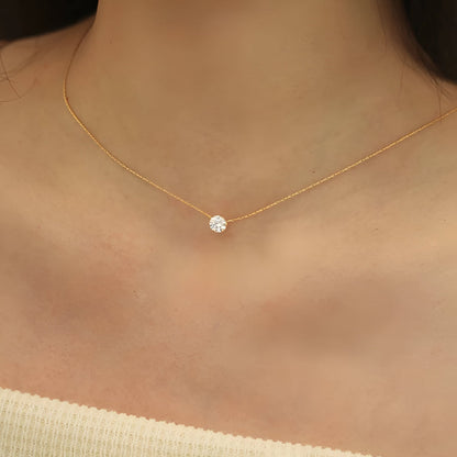 Pendentif solitaire en acier doré et diamant naturel porté au cou d'une femme.