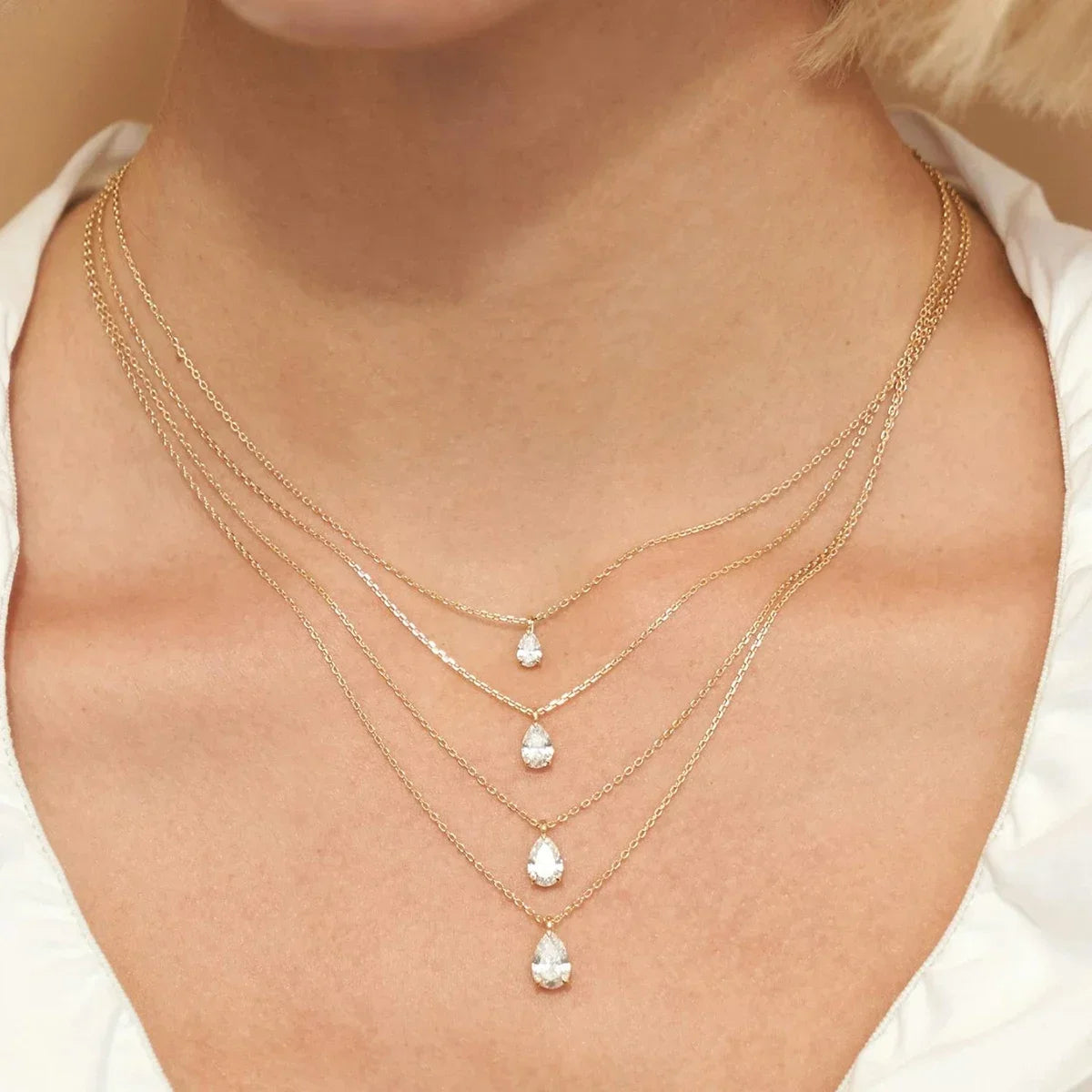 Pendentifs solitaire goutte en or jaune et diamant synthétique portés au cou d'une femme.