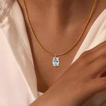 Pendentif solitaire ovale en or jaune et diamant synthétique porté au cou d'une femme.