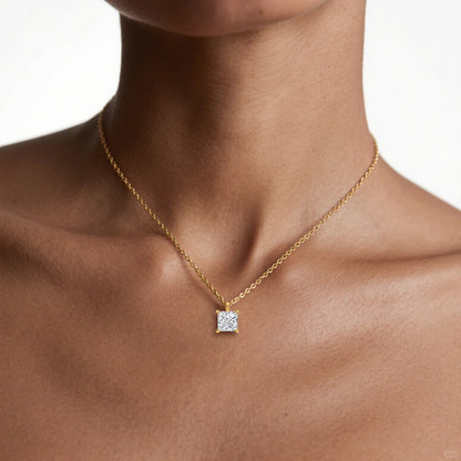 Pendentif solitaire princesse en or jaune et diamant synthétique porté au cou d'une femme.