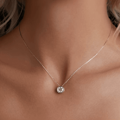 Pendentif solitaire serti clos en or blanc de haute qualité et diamant synthétique 1ct porté au cou d'une femme vue de proche.