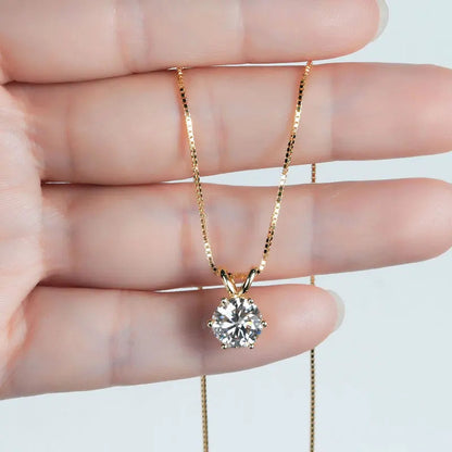 Pendentif solitaire serti six griffes en argent 925 plaqué or jaune et diamant étincelant montré entre les doigts d'une femme vue de proche.