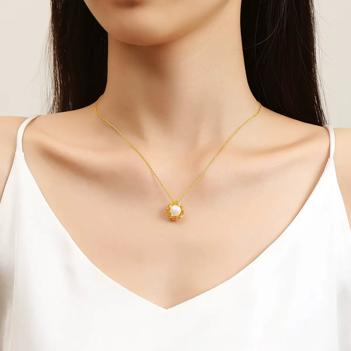 Pendentif fleur de tournesol Florina en or jaune 18K rayonnant et perle nacrée porté au cou d'une femme vue de face.