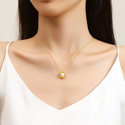 Pendentif fleur de tournesol Florina en or jaune 18K rayonnant et perle nacrée porté au cou d'une femme vue de face.