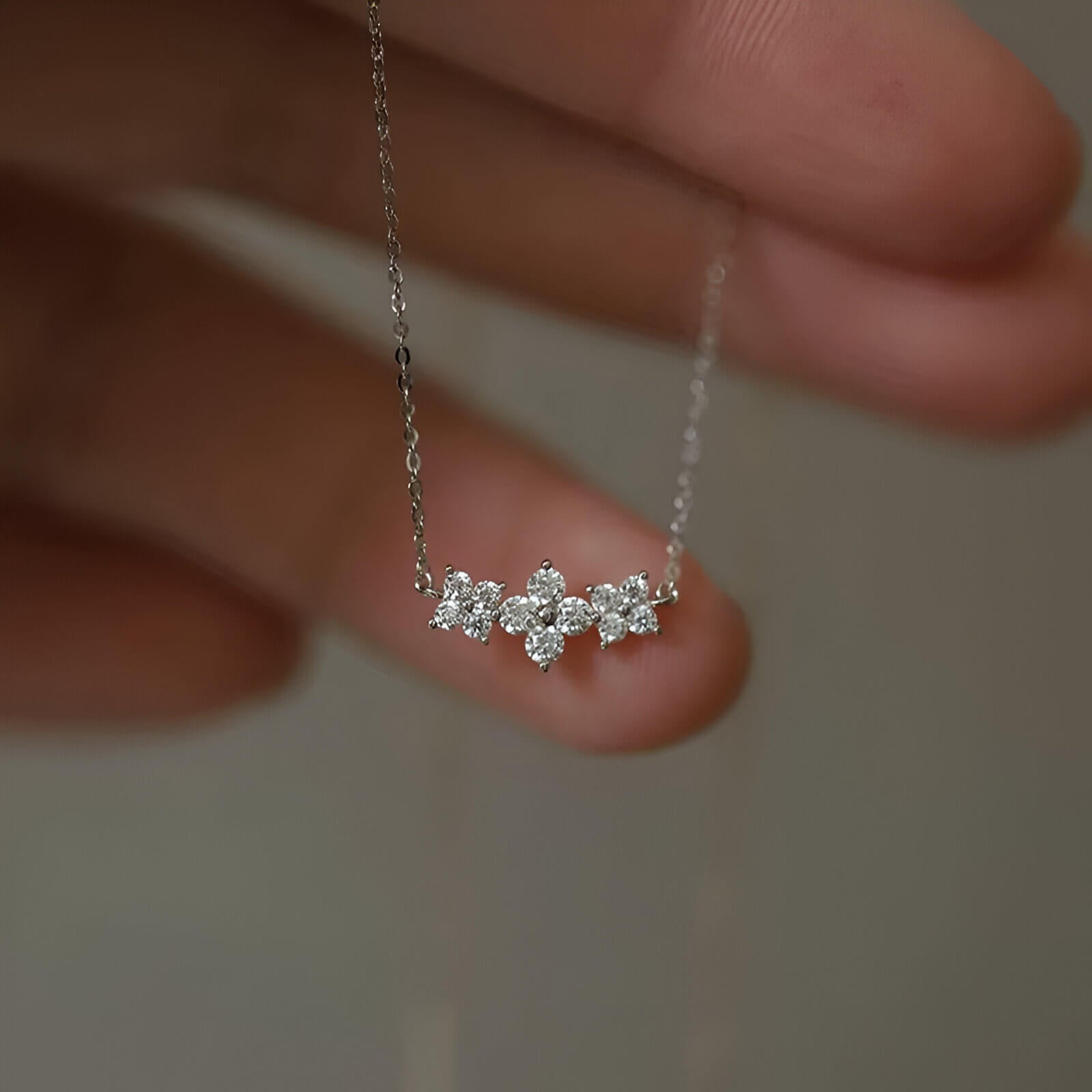 Pendentif trio de fleurs en argent 925 plaqué or blanc raffiné et diamants montré entre les doigts d'une femme vue de face.