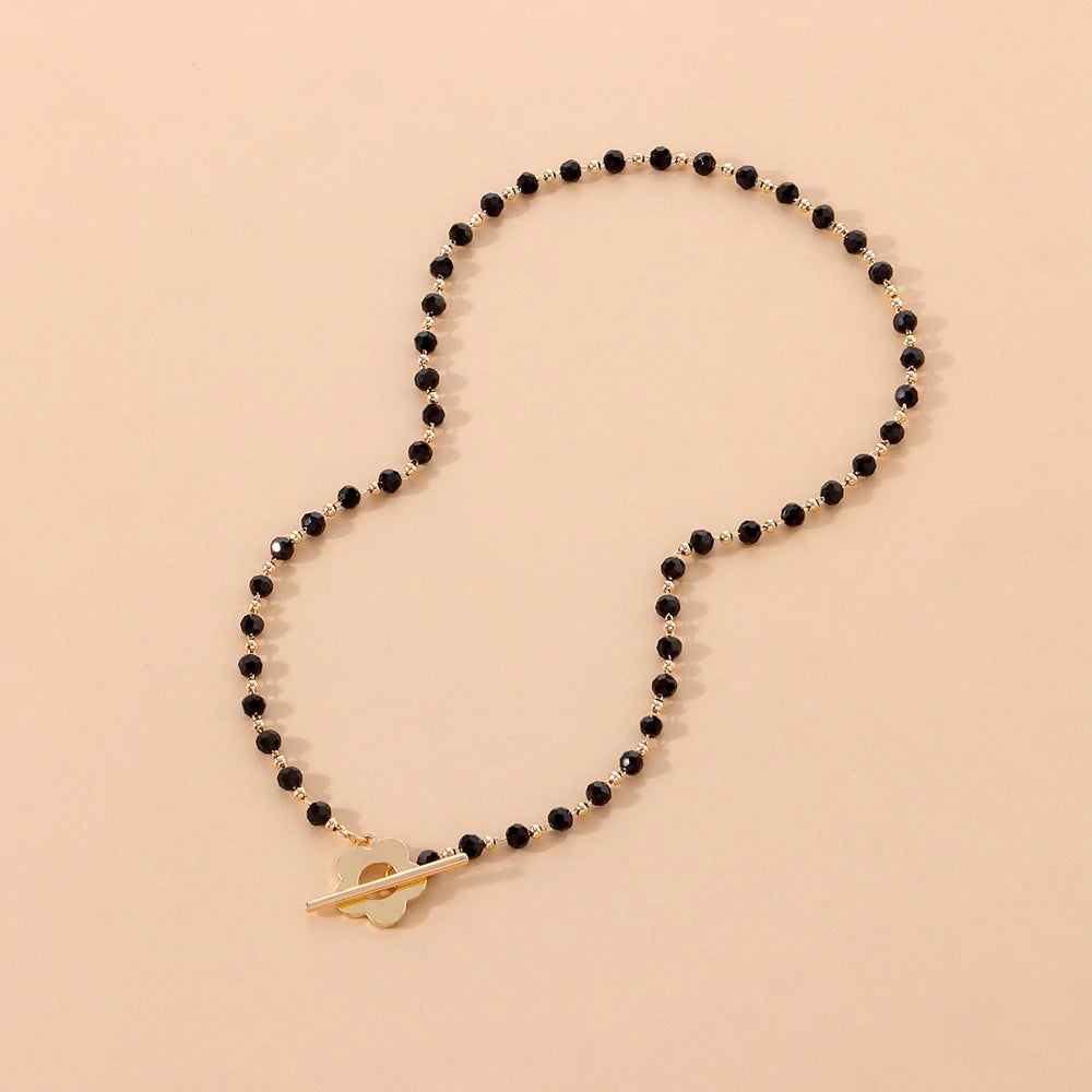 Collier ras-du-cou fleur de marguerite en plaqué or jaune et cristaux noirs en entier à plat.