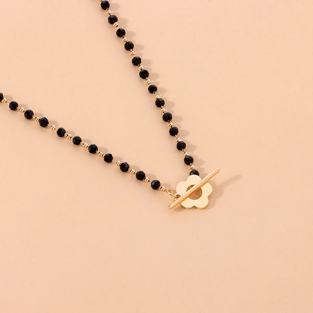 Collier ras-du-cou fleur de marguerite en plaqué or jaune et cristaux noirs à plat.