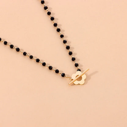 Collier ras-du-cou fleur de marguerite en plaqué or jaune et cristaux noirs à plat.