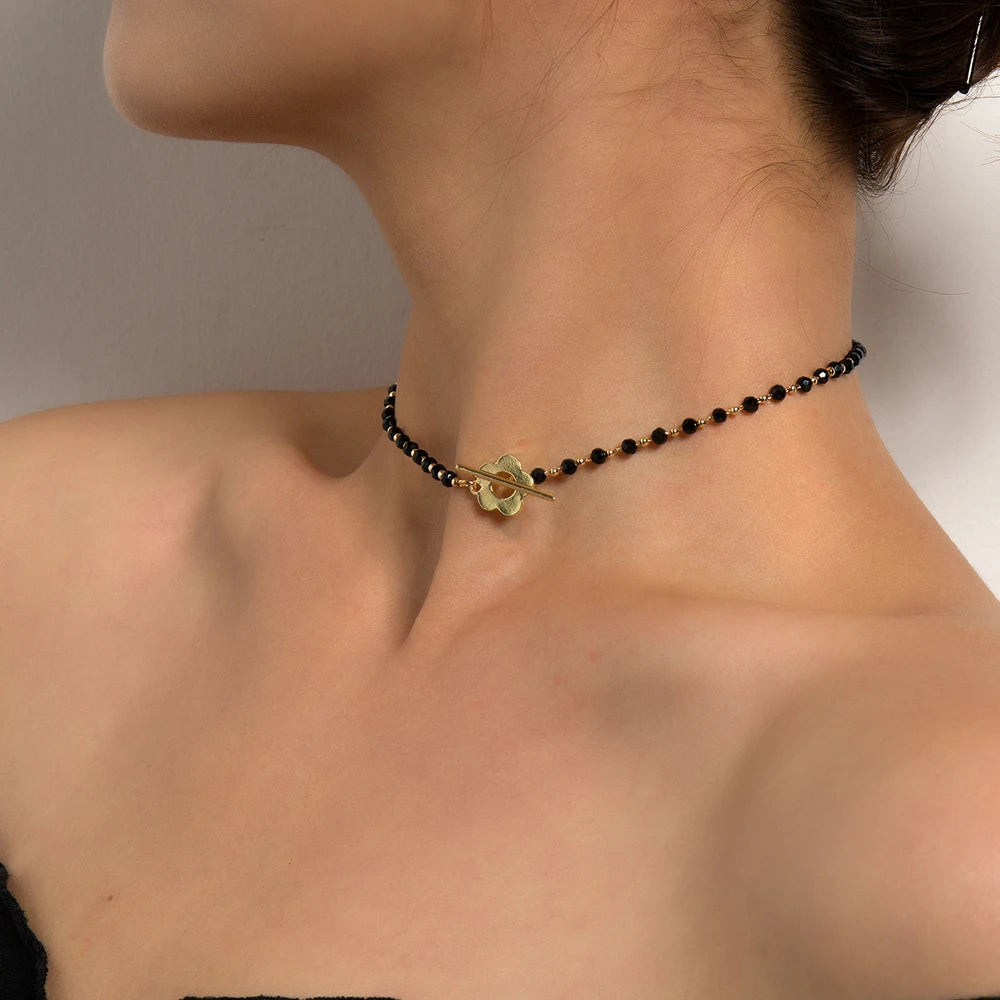 Collier ras-du-cou fleur de marguerite en plaqué or jaune et cristaux noirs porté au cou d'une femme vue de côté.